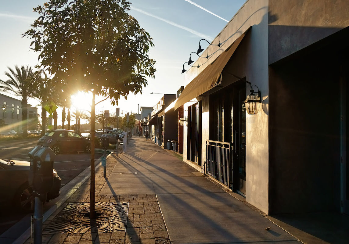 Storefronts along a city street lined with trees and cars.